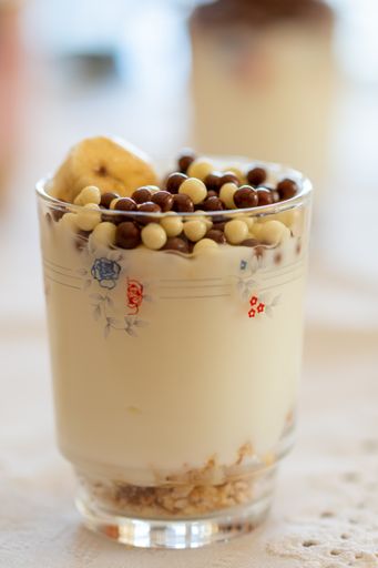 A vertical shot of a delicious healthy dairy dessert with bananas, cereal, and candies in a glass