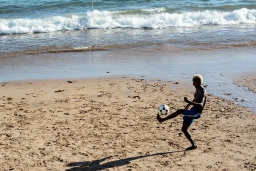 Young model playing sand football on the beach under strong summer sun. Salvador Bahia Brazil.