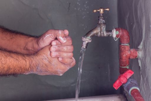 A man washing his hands with neutral soap and water in a poor toilet