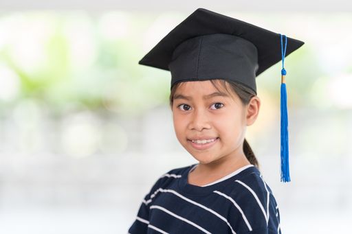 A shallow focus shot of a happy Thai kid with a graduation hat