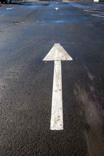 A vertical shot of a white directional arrow in a parking lot