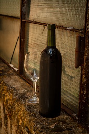 A vertical shot of a bottle of red wine and empty wineglass on an aged windowsill