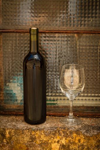 A vertical shot of a bottle of red wine and empty wineglass on a retro windowsill