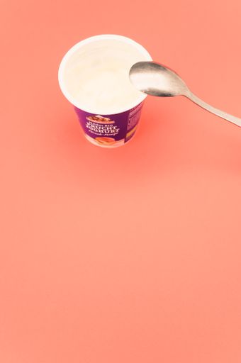 isolated half full organic fruits yogurt cup and spoon on a salmon tabletop with copy space