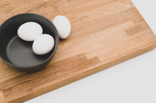 organic white eggs in a dark gray bowl and wooden chopping board on a white surface with copy space for text