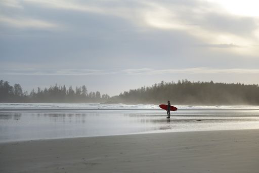 A man with a surfboard standing on Long Beach, Pacific Rim National Park, British Columbia, Canada.