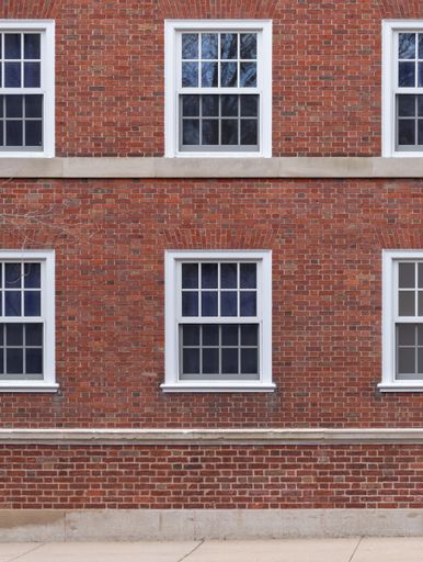 A vertical shot of the identical white windows of a red cobblestone building