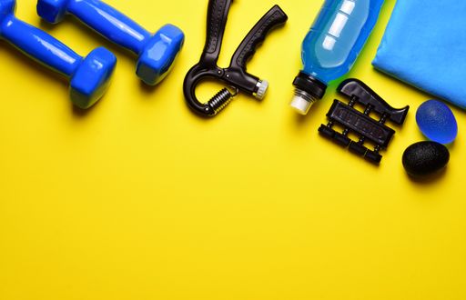 A top view of fitness tools. The bottle, hand and finger grips, and dumbbells isolated on a yellow background