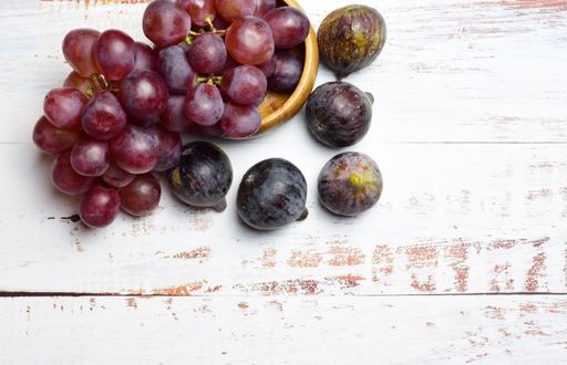 A top view of ripe purple figs and grapes isolated on white wooden background