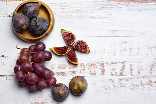 A top view of ripe purple figs and grapes isolated on white wooden background