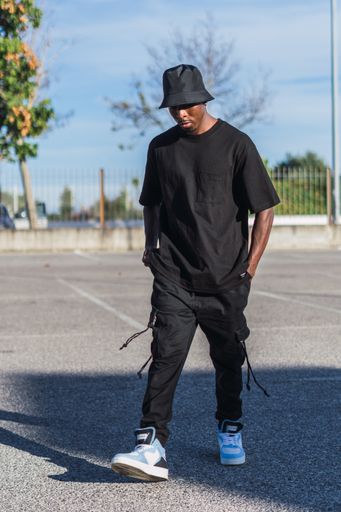 A vertical shot of a young black man in street-style clothes walking outdoors on a sunny day