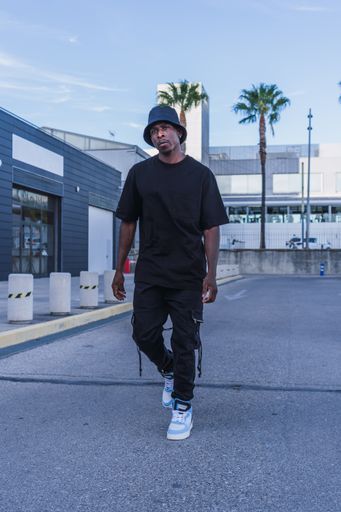 A vertical shot of a young black man in street-style clothes confidently walking outdoors