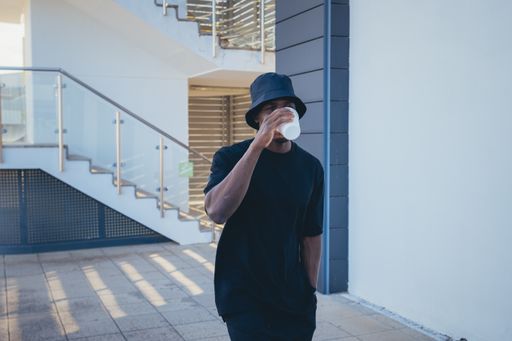 A young black man in street-style clothes drinking his takeaway beverage outdoors