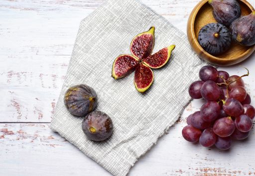 A top view of ripe figs and red grapes on the checkered fabric and grunge wooden background