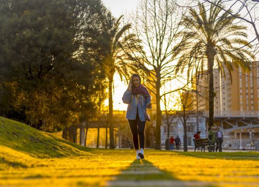 A young female walking through a park and talking on the phone during the golden hour in Bilbao, Spain