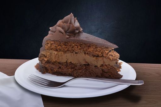 A decadent slice of chocolate cake with rich frosting on a white plate and fork, set against a dark background.