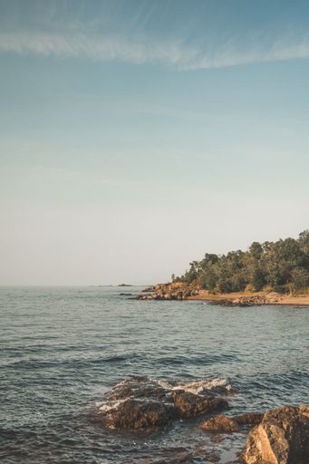 Scenic coastal view with rocky shoreline and lush greenery under a clear blue sky, capturing the tranquility of nature.