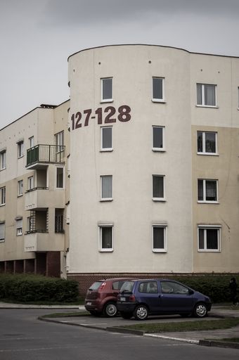 A vertical shot of two parked cars in front of an apartment building in the Stare Zegrze district