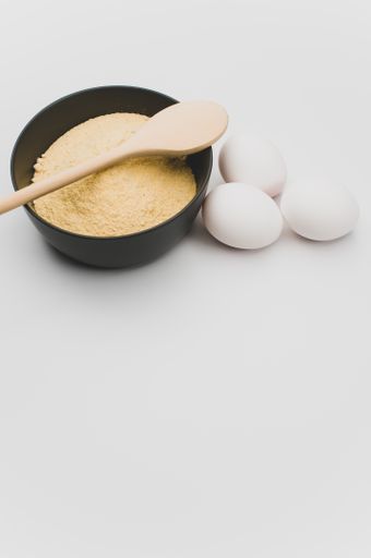 wooden spoon white eggs and dark gray bowl with wholegrain flour on white background with copy space
