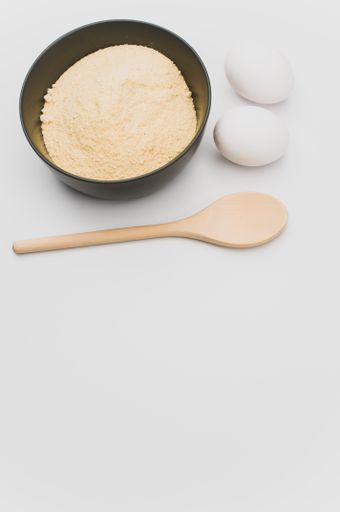 wooden spoon white eggs and dark gray bowl with wholegrain flour on white background with copy space