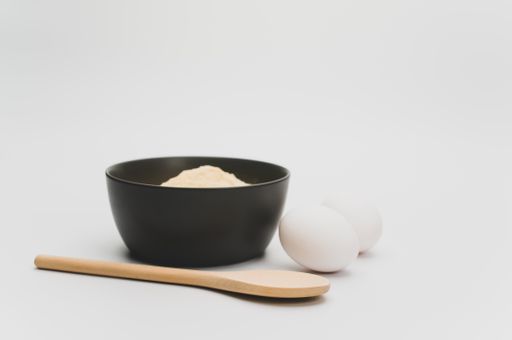 wooden spoon white eggs and dark gray bowl with wholegrain flour on white background with copy space