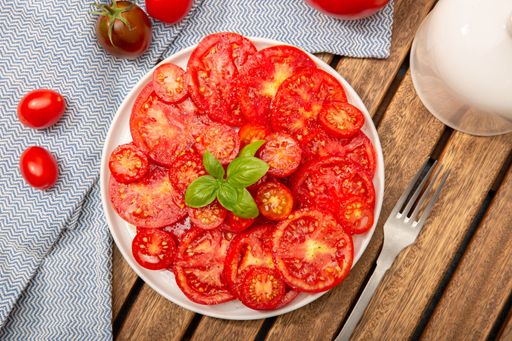 Top view of Sliced tomatoes seasoned with oil, salt and pepper, garnished with basil leaves on a white plate