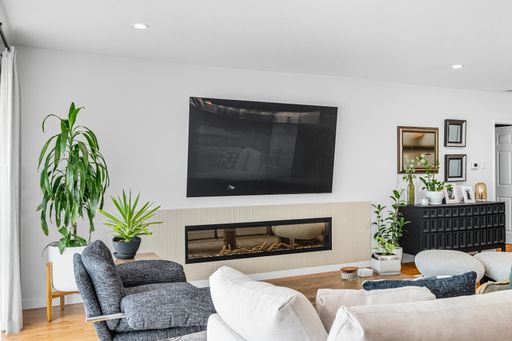 Contemporary living room with mounted TV, built-in fireplace, neutral tones, and bright natural light through sheer curtains