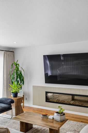 Contemporary living room with mounted TV, built-in fireplace, neutral tones, and bright natural light through sheer curtains