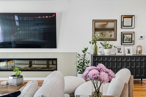 Contemporary living room with mounted TV, built-in fireplace, neutral tones, and bright natural light through sheer curtains