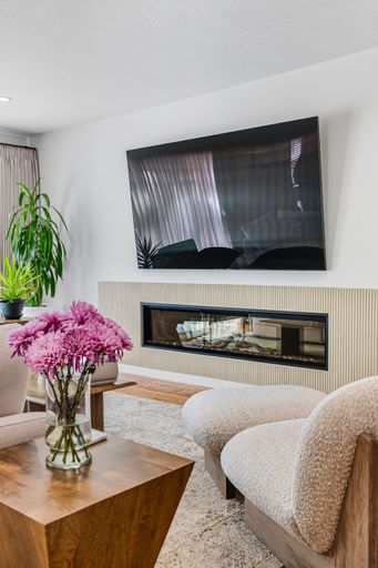 Contemporary living room with mounted TV, built-in fireplace, neutral tones, and bright natural light through sheer curtains