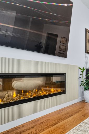 Contemporary living room with mounted TV, built-in fireplace, neutral tones, and bright natural light through sheer curtains
