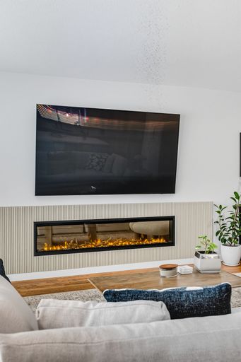 Contemporary living room with mounted TV, built-in fireplace, neutral tones, and bright natural light through sheer curtains