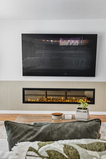 Contemporary living room with mounted TV, built-in fireplace, neutral tones, and bright natural light through sheer curtains