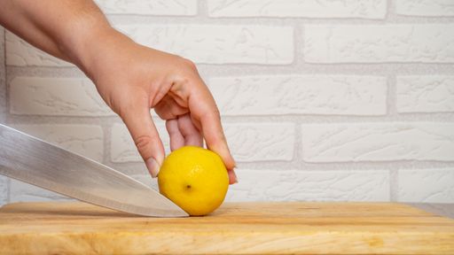 A hand holding a bright yellow lemon with the brick wall in the background