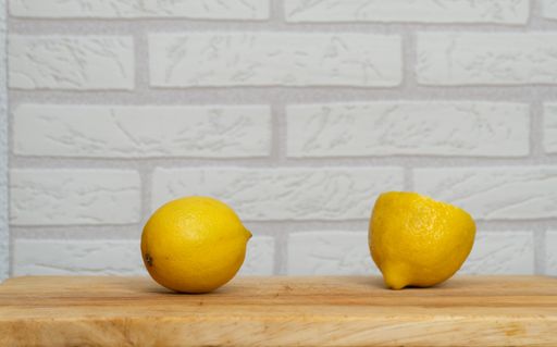 The two bright yellow lemons on the table with the brick wall on background