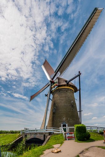 Windmill in Kinderdijk, Netherlands. A blue sky with some nice clouds. A small bridge and the typical Dutch shoes at the base of the mill.