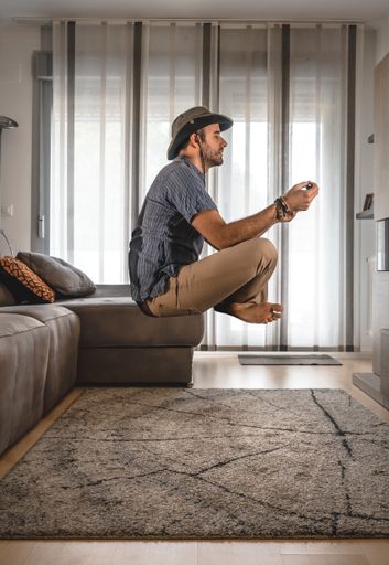 A vertical shot of a male meditating and floating in the air in his living room