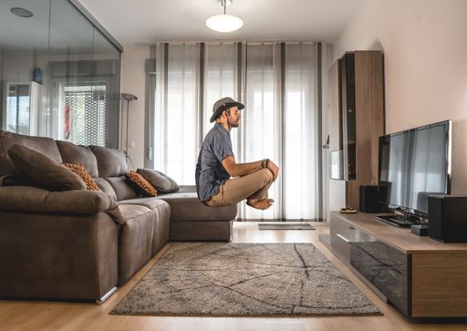 A male meditating and floating in the air in front of the TV in the living room
