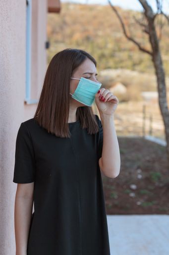 A vertical shot of a Caucasian female coughing while wearing a face mask during the covid-19 pandemic