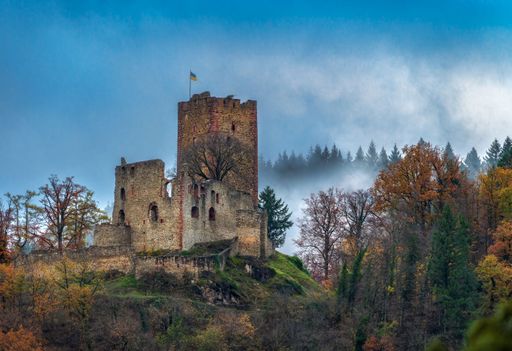 An ancient castle ruin surrounded by autumn trees and mist in a serene landscape.