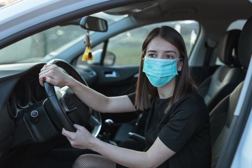 A Caucasian female in a face mask driving a car