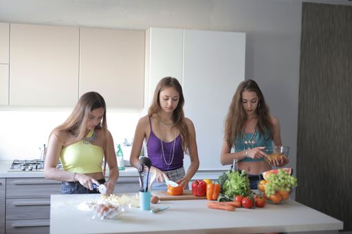 A  beautiful shot of 3 females preparing a meal in a kitchen with ingredients on white table