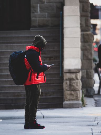 A vertical shot of a lonely man in a red coat scrolling down on his phone in Calgary,Canada.