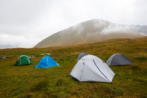 Colorful tents set on a grassy hillside with a misty mountain backdrop, creating a serene camping scene.