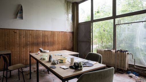 A glass window with a messy table inside of an abandoned room of a building