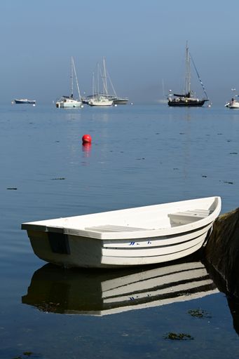 A serene seascape featuring a small white boat and distant sailboats under a clear blue sky, reflecting tranquility and calmness.