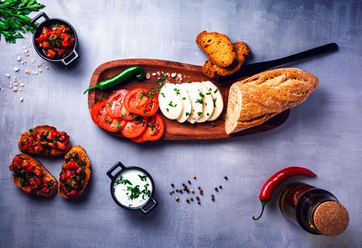 A top view of an Italian antipasto platter with sliced tomatoes, mozzarella, bread, and bruschetta on a gray background.