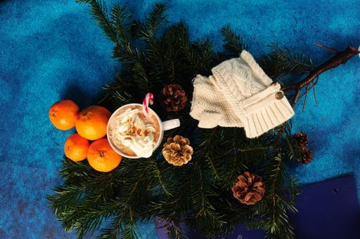A top view of Christmas decorations with hot chocolate, oranges, and white mittens