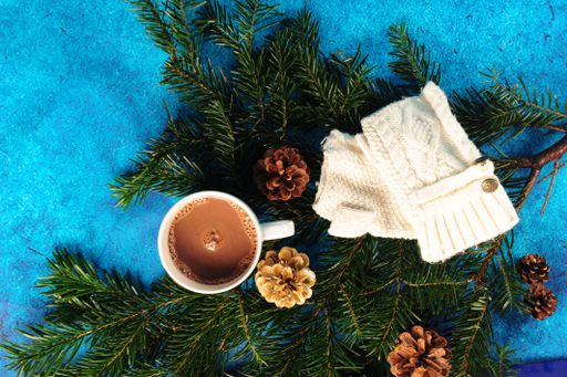 A top view of pine, fir twigs, white mittens, and hot chocolate on a blue background