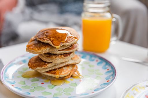 A stack of pancakes with dripping maple syrup and a glass of fresh orange juice